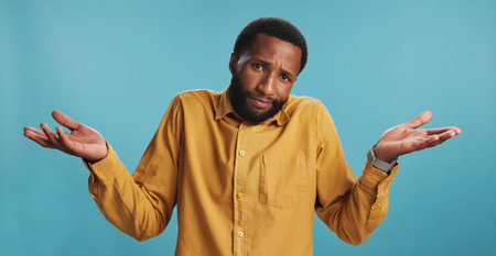 Portrait, confused black man and shrug in studio for choice, decision or option comparison on blue background. Face, doubt and puzzled person with palm gesture for question, why and dont know emojiの写真素材