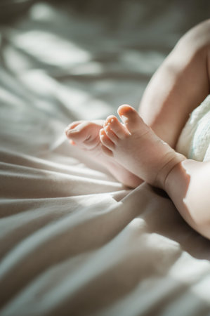 Baby, feet and infant relax lying on a bed in a bedroom with sun, sunlight or sunshine in the...