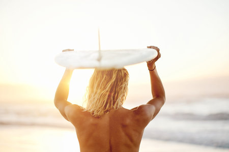 Back, surfing and sport with a man on the beach, holding his surfboard over his head in the water....
