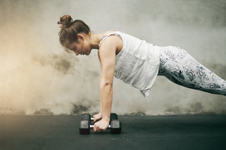 Fitness, woman and push ups in weightlifting for exercise, intense workout against urban background. Sporty, fit or active female with dumbbells or training core or ab muscles for strength exercisingの写真素材