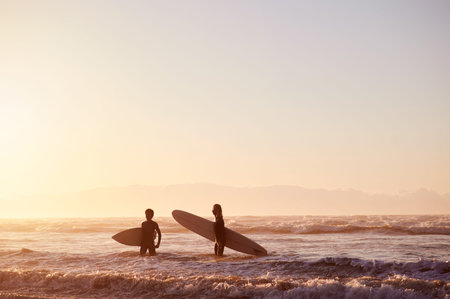 Sunset, beach and silhouette of men with surfboard walking in waves together on surf holiday in...
