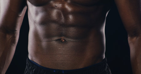 Abs, muscles and torso of man in studio with sweating for bodybuilding workout. Sports, strength and shirtless African athlete with six pack for exercise, challenge or training by black background.の写真素材