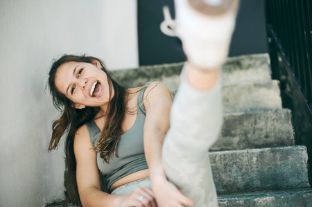 Happy, city and portrait of fitness woman on stairs and relaxing after fun exercise, training and cardio workout with kick. Smile, sports and young playful girl with confidence and kicking by stepsの写真素材