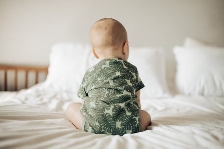 Baby, back view and infant sitting on a bed in a bedroom relax in development in as home or house being cute and curious. Toddler, child or kid in a nursery relaxing enjoying childhood and playingの写真素材