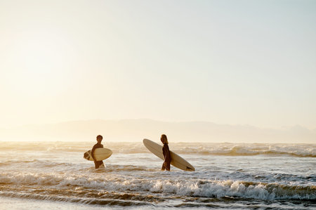 Sunset, beach and men with surfboard walking in waves together in evening on surf holiday in Hawaii....