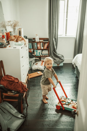 Cute, toys and boy toddler playing in his nursery for child development and fun at home. Playful, sweet and portrait of a little infant kid walking with a wood barrow in his bedroom in the house.の写真素材