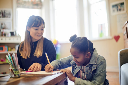 Learning, adoption and mother with black girl writing in home for homework, drawing and homeschool. Development, studying and mama helping happy foster kid or student with education on clipboard.の写真素材