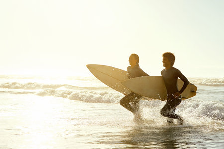 Travel, sunset and couple running on the beach with surfboards to practice surfing while on...