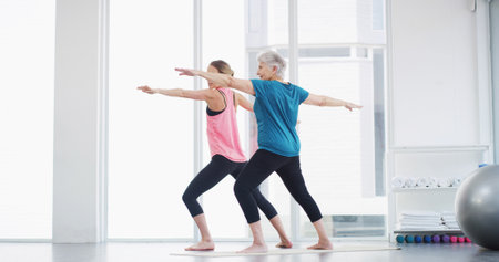Yoga, senior woman and coach for fitness, healthy body and warrior pose for geriatric wellness. Stretching, pilates trainer and exercise together for balance, physical therapy and holistic in gymの写真素材