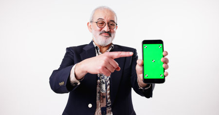 Studio, green screen and mature man with smartphone, space or pointing for presentation of mobile. White background, tips and advertising of web application, tracking markers or display of technologyの写真素材