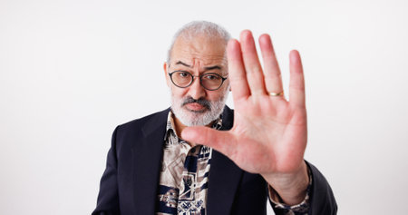 Portrait, senior man and hand gesture for stop in studio of conflict warning, sign language and danger. Elderly interpreter, limit and attention for protest caution, news control and white backgroundの写真素材