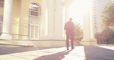 Back, business and man walking in city of real estate travel, showcase viewings and morning commute. Professional, male consultant and urban explore for commercial property, infrastructure conditionsの写真素材