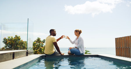 Travel, hotel and couple cheers at pool for tropical vacation with drinks, relax and happy bonding together. Cocktail, man and woman at beach resort with toast, smile and love on island holidayの写真素材