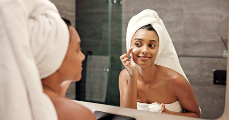 Bathroom, mirror and woman with cream for skincare, wellness and anti aging benefits in morning. Home, reflection and female person with smile for cosmetics, beauty treatment and moisturizer for faceの写真素材