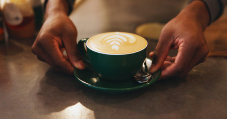 Hands, latte art and presentation with barista at coffee shop counter for hospitality or service closeup. Creative, cup and drink with care or restaurant employee in startup cafe for small businessの写真素材