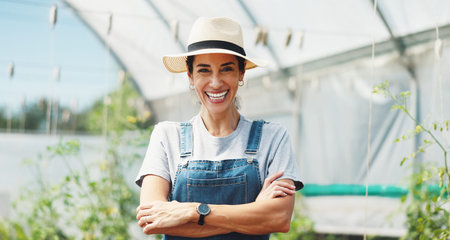 Woman, smile and arms crossed in greenhouse, farming and growth with sustainability in summer. Person, happy and portrait with food production, agriculture and nursery for vegetables in Portugalの写真素材