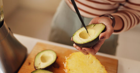 Woman, hands and avocado for smoothie in home, prepare organic shake and cutting ingredients. Person, breakfast fruit and minerals for gut health nutrition in kitchen, vegan diet and morning fiberの写真素材