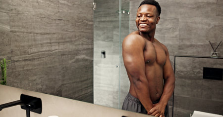 Happy, black man and mirror for flexing in bathroom of fitness progress, muscle growth and workout pride. Smile, male person and reflection of strong biceps, grooming routine and bodybuilder at houseの写真素材