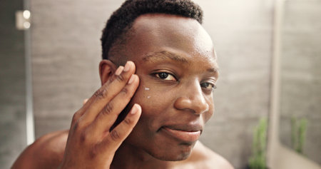 Eye cream, skincare and face with black man in bathroom for beauty, morning routine and cosmetics. Treatment, hotel resort and cleaning with person at home for grooming, spa glow and self careの写真素材