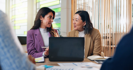 Business women, laptop and documents at startup, meeting and discussion for budget review, revenue and profit. People, diversity and talk in office, charts and finance management at creative agencyの写真素材