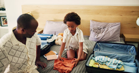 Packing, dad and child with luggage, vacation and preparing for holiday with parent, black man and travel. House, kid and helping father with baggage, clothes and family with suitcase for journeyの写真素材