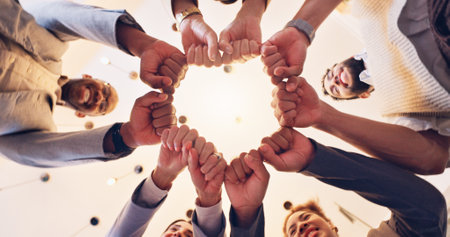 Happy, business people or meeting with fist bump below for unity, motivation or teamwork at office. Low angle, employee or group with touch, smile or trust for mission, synergy or solidarity togetherの写真素材