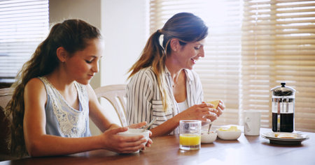Breakfast, mom and child with food, home and bonding in dining room with nutrition, woman and daughter. Eating, mother and kid with healthy diet in apartment, kitchen and family with meal in morningの写真素材