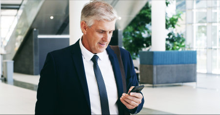 Phone, travel and reading with business man in airport for Conference trip schedule, itinerary and networking seminar. Online agenda, app and hotel booking with mature person at terminal for check inの写真素材