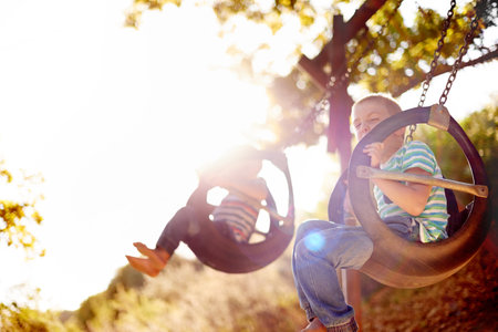 Development, growth and boy child on swing in playground, having fun with activity, games or play. Adrenaline, excited and hanging with smile of happy kid with brother outdoor at park in summerの写真素材