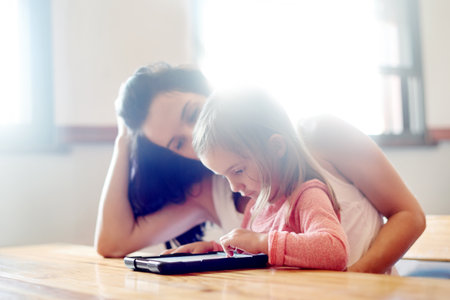 Mother, daughter and learning with tablet in home for online education, watching cartoon or child development. Woman, girl or tech for streaming subscription, reading support or gaming app with flareの写真素材