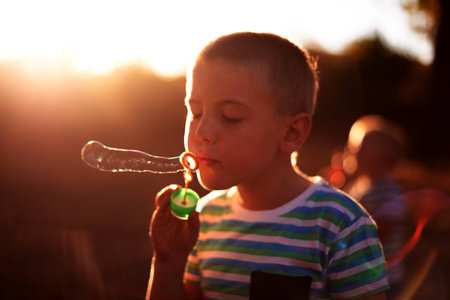 Bubbles, blowing and child in park with fun, sunset adventure and outdoor development for kids in nature. Relax, weekend and boy in garden playground with soap wand, childhood games and play activityの写真素材