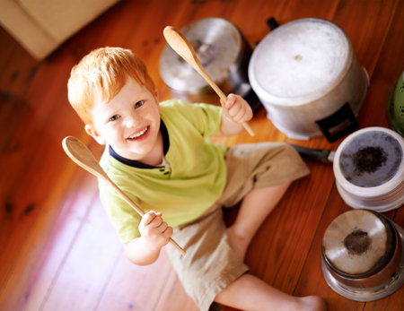Drummer, portrait and pots with smile of boy on wooden floor in home living room from above. Cookware, crockery and instrument with happy child in apartment for fantasy, imagination or playing musicの写真素材