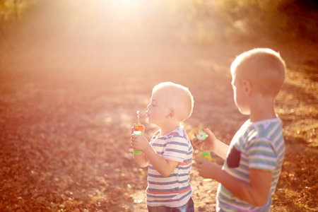 Happy, blowing bubbles and children in park for fun, childhood and bonding together outdoors....