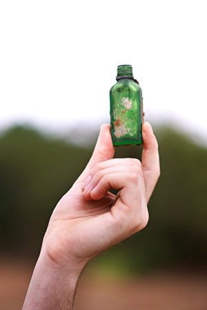 Person, hand and bottle in nature for recycle, social responsibility and environment care. Man, volunteer and outdoor with glass vial to collect rubbish, cleaning and Earth Day awareness with ecologyの写真素材