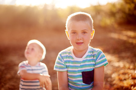 Portrait, nature and brothers in park, game and smile with energy, bonding together and happiness. Face, boys and siblings with joy, lens flare and countryside with childhood development and breakの写真素材