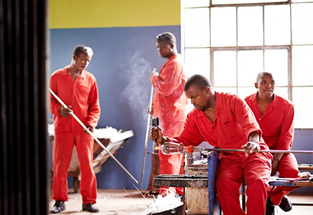 Glassblower, molding and man in factory with production and equipment for professional craft. Labor, workshop and person shaping object with tools for metalwork, manufacturing and forge for heatingの写真素材