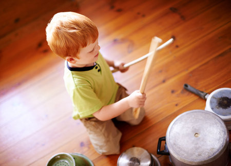 Home, playing and child with pots, drumming and noise with cookware on floor, musician and performance. Song, drummer and kid with wooden spoon for fun, sound or improved coordination of boy in houseの写真素材