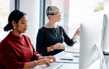 Business women, consultant or agency with headset for customer service, telemarketing or online advice at office. Female people, team or agent consulting with computer for telecommunications or salesの写真素材