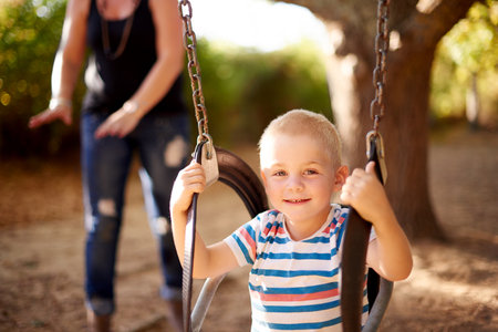 Smile, swing and portrait of kid in park with play, outdoor adventure and child development in nature. Relax, mother and happy boy in playground for growth, fun games or playful childhood on weekendの写真素材