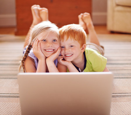 Watching, siblings and children with laptop, floor and education with videos, learning and thinking. House, sister and brother with knowledge in living room, growth or development for youth with infoの写真素材