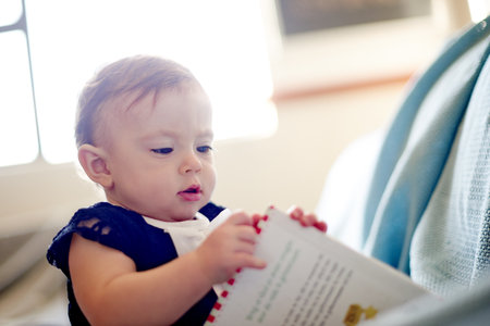 Baby, girl and playing with book for story, childhood or youth in development at home. Little child, kid or adorable infant with novel for learning, curiousity or imagination in nursery at houseの写真素材