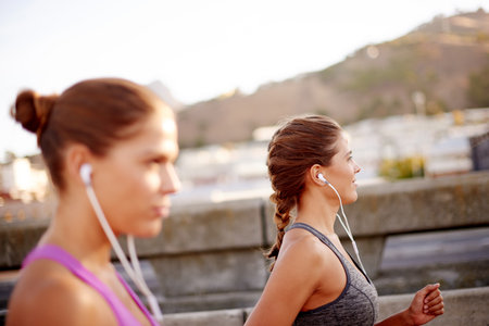 Music, running and fitness with women in city for health podcast, workout and exercise playlist. Runner, wellness and earphones with people training for sports athlete, twin sister or marathonの写真素材