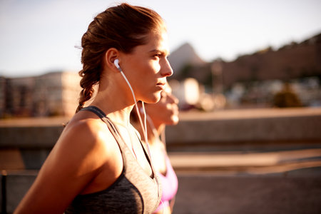 Earphones, running and race with women in city for health podcast, workout and exercise playlist. Runner, wellness and music with people training for sports athlete, fitness or marathon practiceの写真素材