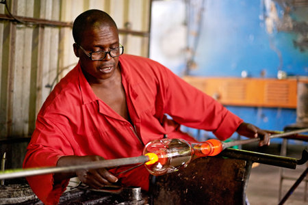 Glass, art and black man in craft workshop for small business with heat, tools and technique. Creative, handmade product and glassblower in factory for sustainable process, design or bottle sculptureの写真素材