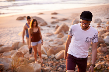 Man, people and walking on beach outdoor for travel, summer adventure and getaway. Group of friends, trekking and ocean trip of holiday journey, tropical destination and bonding together of gatheringの写真素材