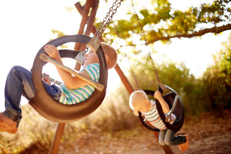 Tree, swing and children in park with play, outdoor brothers and development for kids in nature. Relax, weekend and boy siblings in playground together for fun, games and playful childhood adventureの写真素材