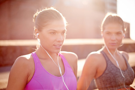 Fitness, music and women with earphones, exercise and training with sportswear in morning and sisters. Twins, athlete and people with routine for wellness, together and healthy with workout in cityの写真素材