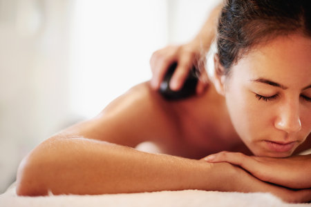 Woman, spa and hot stone massage for back, muscle recovery and stress relief on holiday at resort. Person, masseuse and service with rock for circulation, relax and healing tissue at luxury lodgeの写真素材