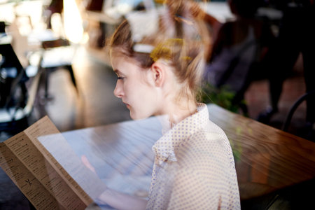 Woman, window and reading menu at coffee shop, hospitality service and paper for food selection. Restaurant, customer search and female person for meal decision, worker and lunch break at bistroの写真素材