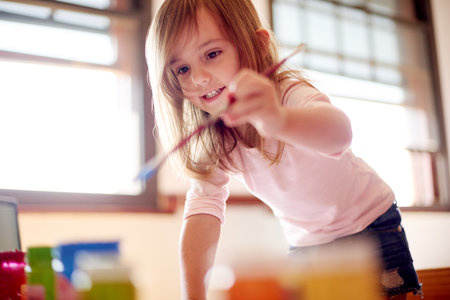 Child, smile and paintbrush in home for creativity, painting and learning with colors. Young girl, playful and brush in living room for artwork, creative outlet and coordination skill developmentの写真素材